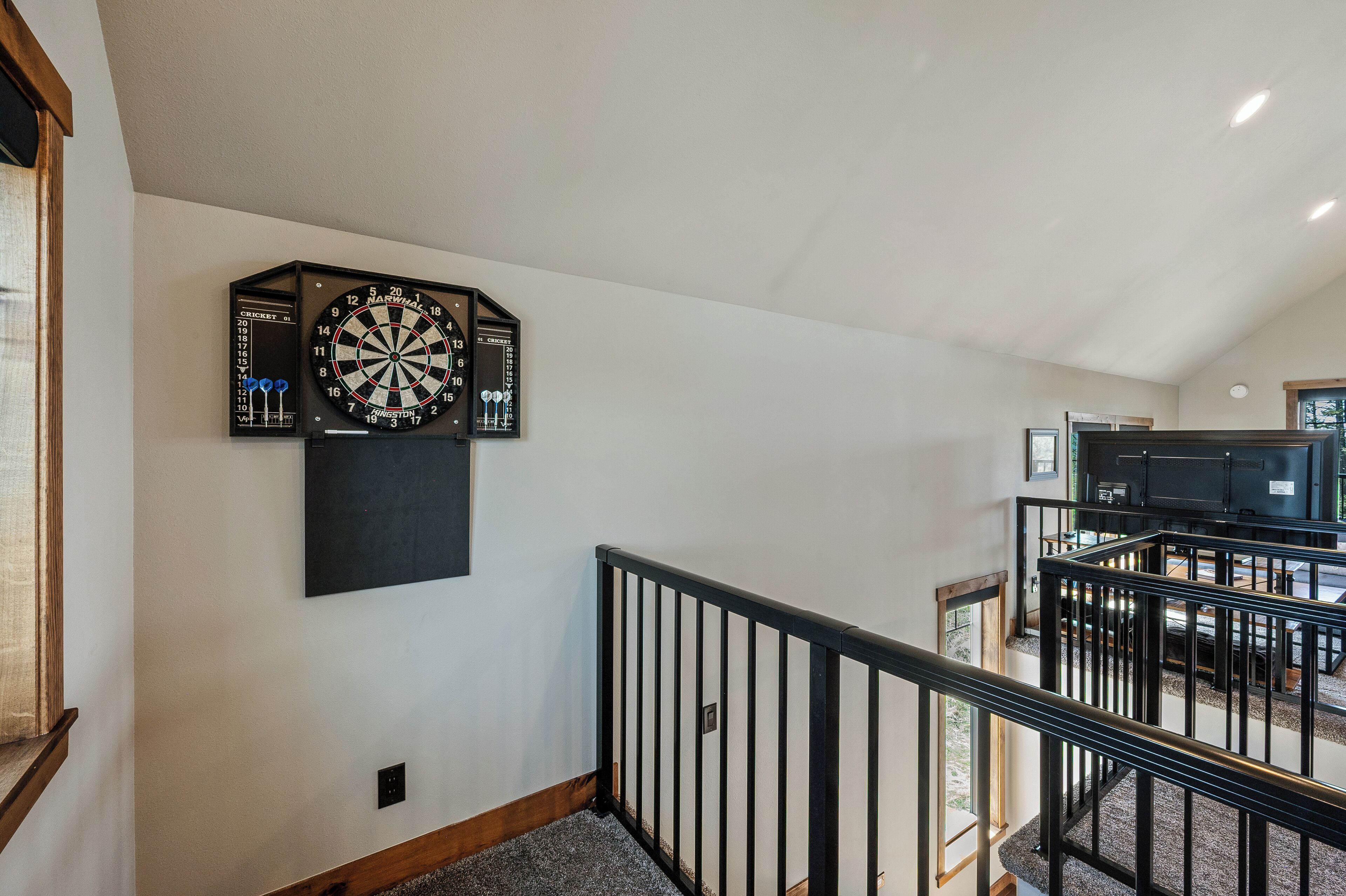 A staircase with a black railing, a dartboard, and a wall-mounted clock.