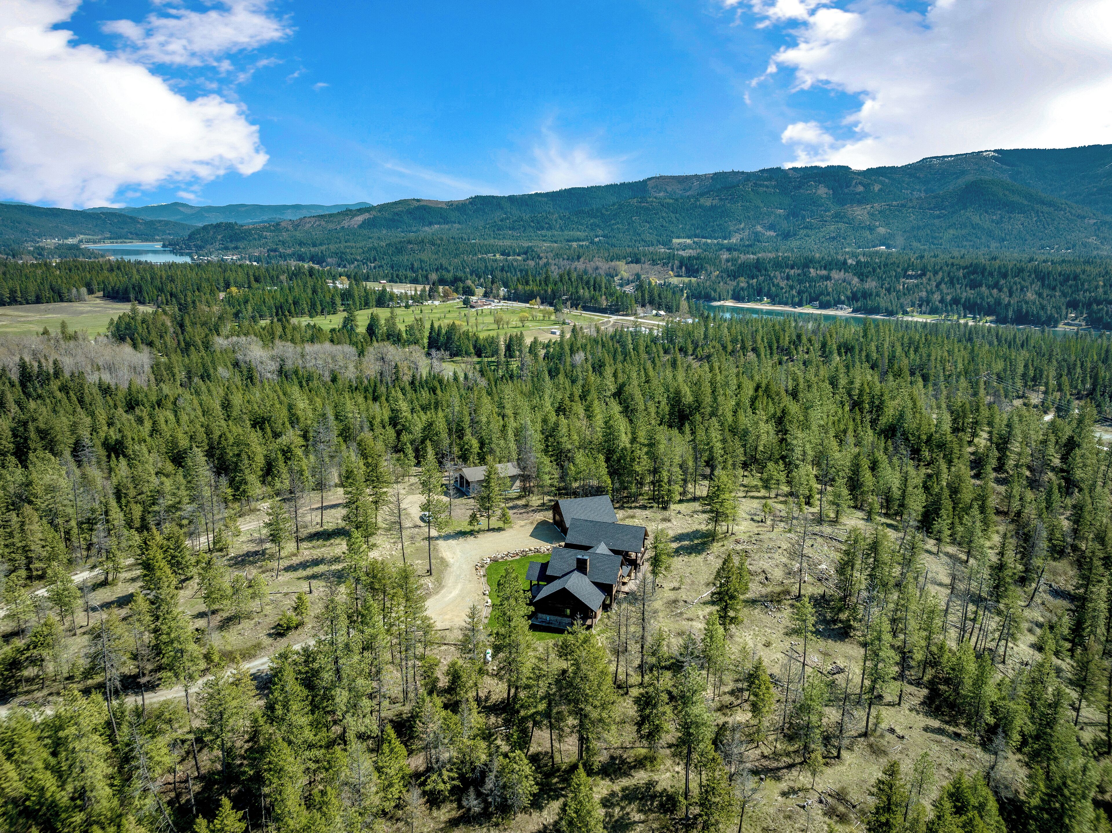 A remote cabin surrounded by dense forest, with a clear view of the surrounding landscape including hills and a lake.