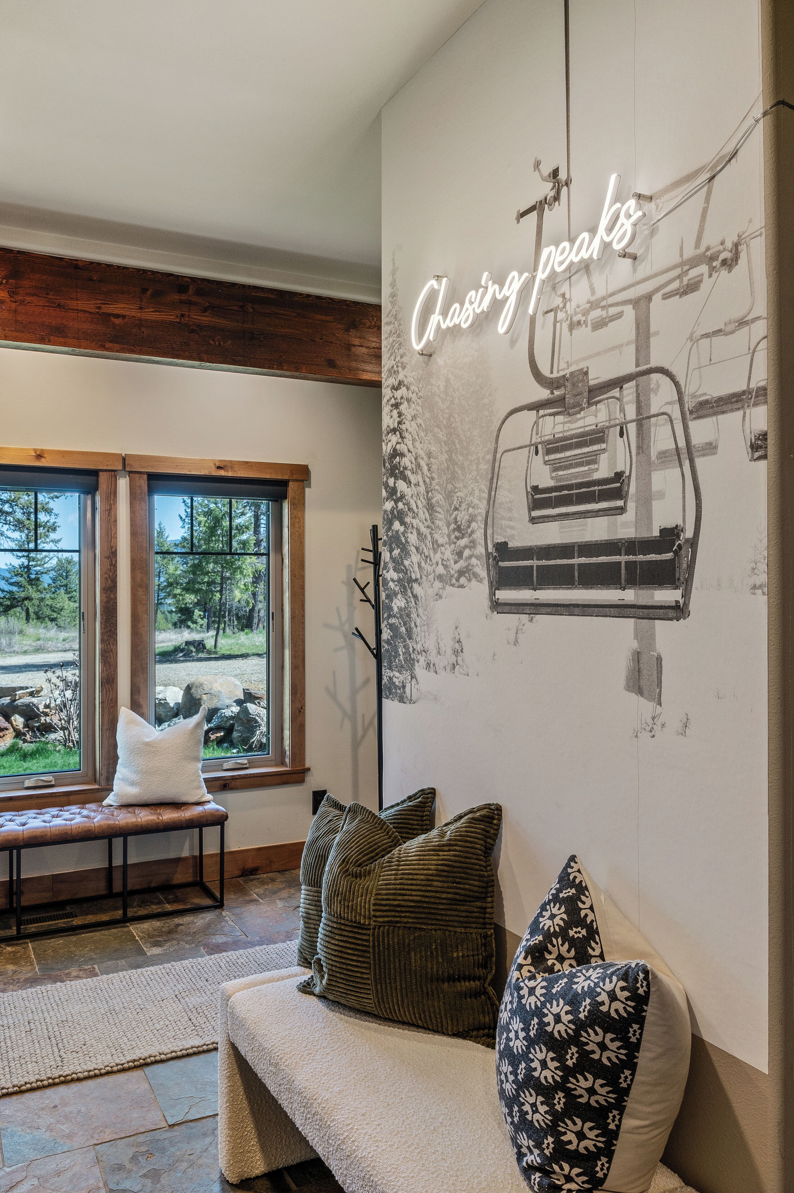 A cozy room with a large window, a bench, and a wall-mounted artwork titled "Climbing peaks".