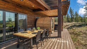 A wooden deck with a dining table and chairs, a large wooden barrel, and a glass door leading to an outdoor seating area.