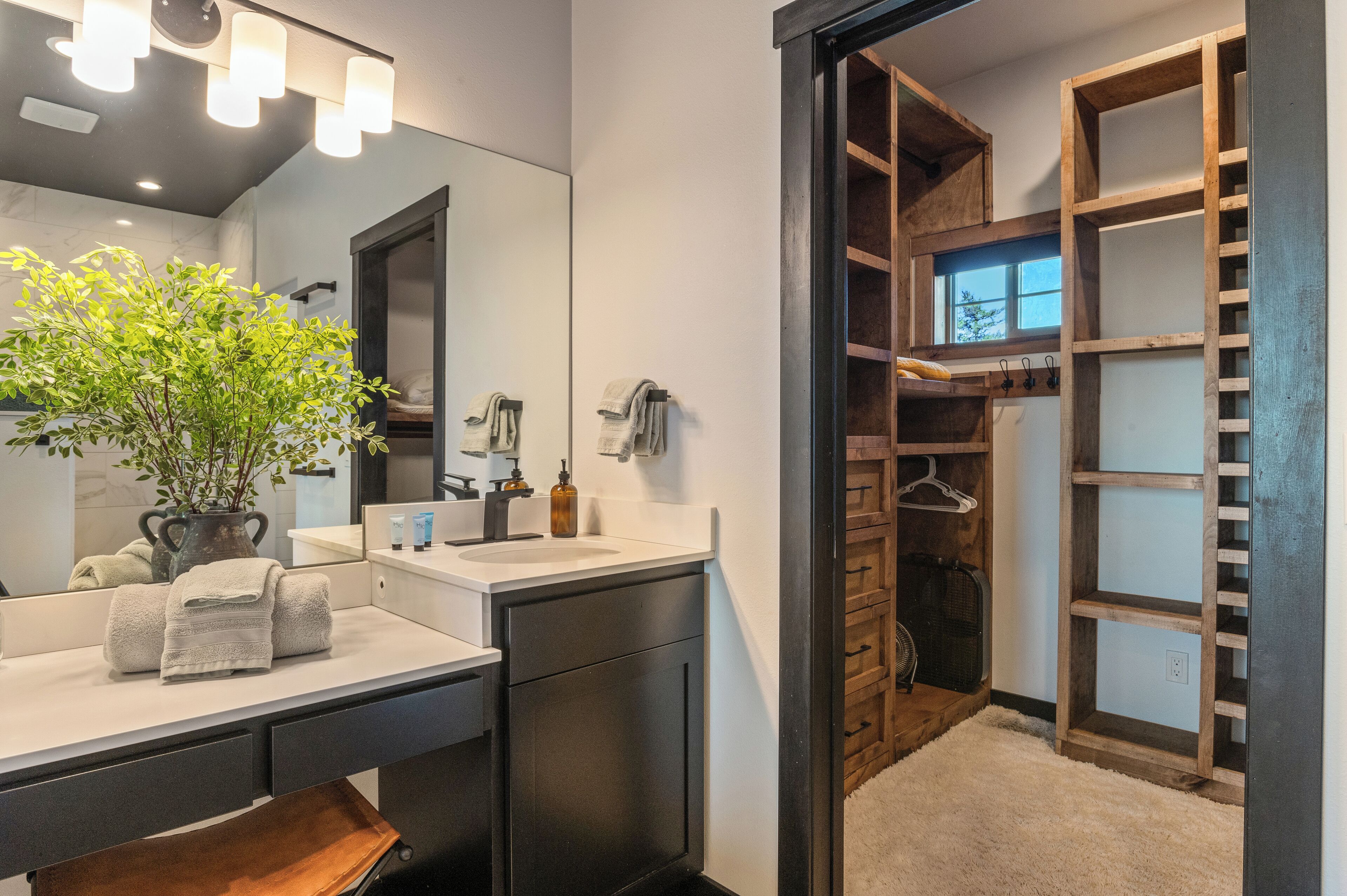 A modern bathroom with a large mirror, a sink with a towel, a plant, and a wooden storage unit.