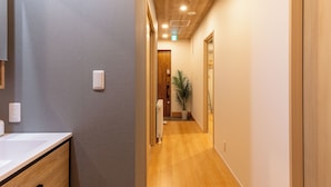 A hallway with wooden flooring, a white wall on one side, and a door at the end. - THE MAISON CHOUCHOU  (Sapporo)