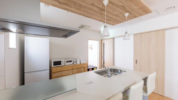 A modern kitchen with a large island, stainless steel appliances, and wooden ceiling beams. - THE MAISON CHOUCHOU  (Sapporo)