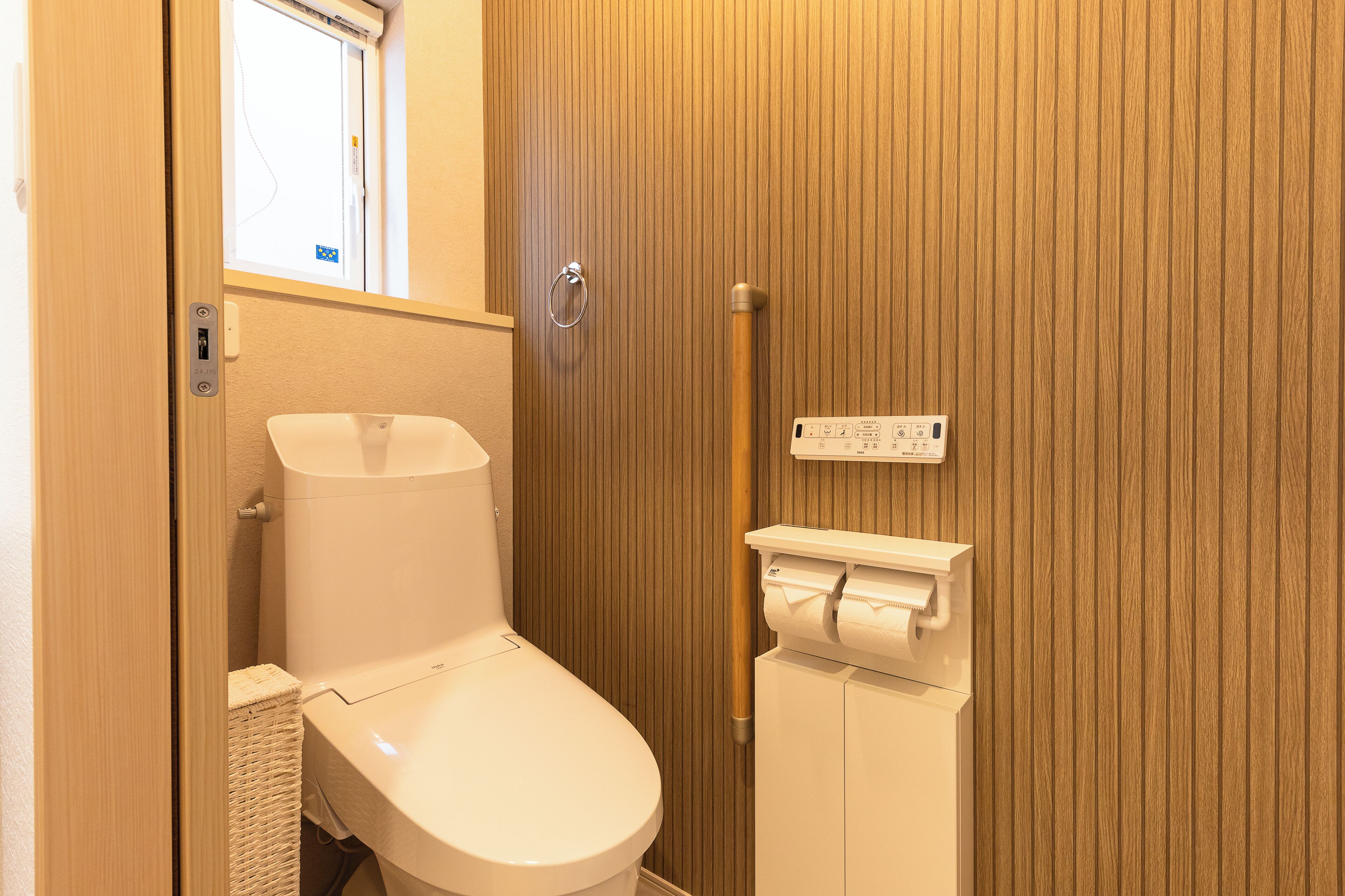 A small, compact bathroom with a toilet, a wooden panel wall, a window, and a towel dispenser.