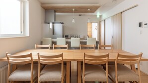 A modern dining area with a wooden table and chairs, a kitchen in the background, and a sliding door closet. - THE MAISON CHOUCHOU  (Sapporo)