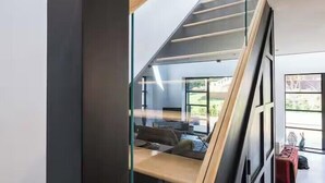 Una escalera moderna con barandas de vidrio y escalones de madera que conduce a una zona de estar superior con vistas al exterior.