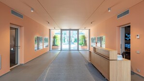 Un hall d’entrée moderne avec un comptoir d’accueil, des portes vitrées donnant sur l’extérieur et des plantes en pot.
