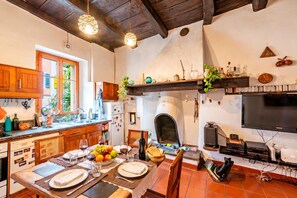 A kitchen with wooden cabinets, a dining table set with plates, glasses, and fruit, a built-in oven, and a TV mounted on the wall.