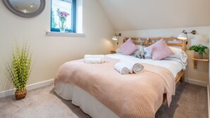 A bedroom with a large bed, a bedside table, a lamp, a mirror, and a window with flowers. - Wayside Loft by Interhome (Drumnadrochit)