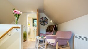 A modern interior with a staircase, a pink armchair, a small table with a teapot, and a clock on the wall. - Wayside Loft by Interhome (Drumnadrochit)