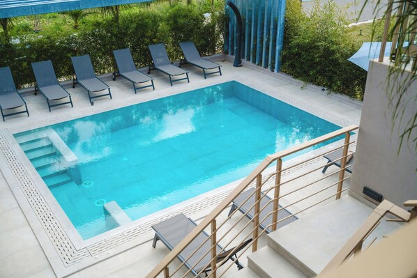 A rectangular swimming pool with a tiled deck, surrounded by lounge chairs and a wooden staircase leading down.