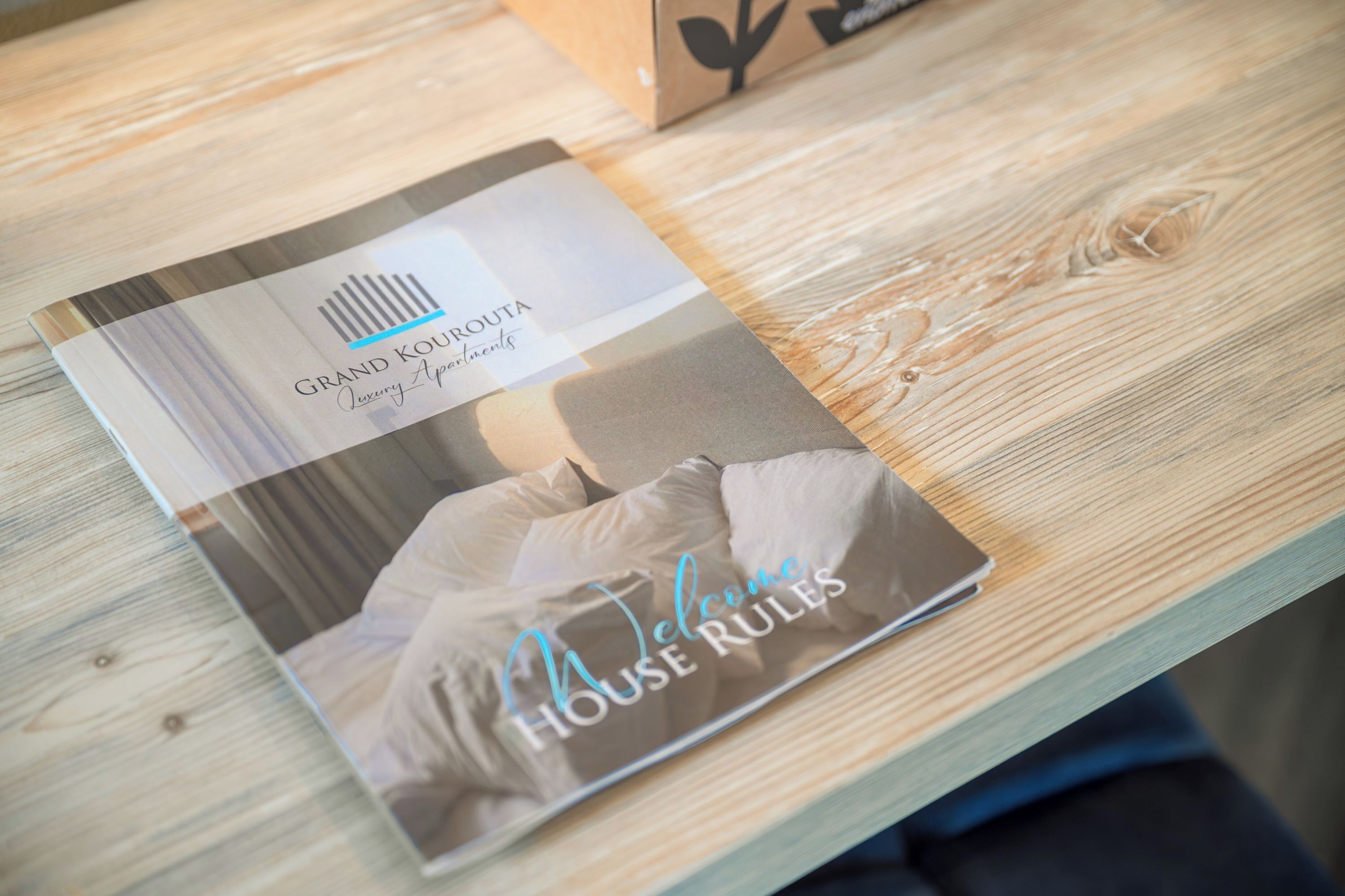 A brochure titled "Grand Kouropta Luxury Apartments" on a wooden table.
