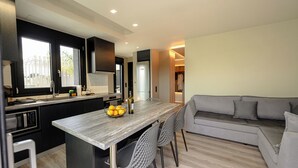 A modern kitchen with a central island, black cabinets, and a grey sofa in the living area. - Kourouta Luxury Suites with Pool nr3, Kourouta, Greece (Kourouta)