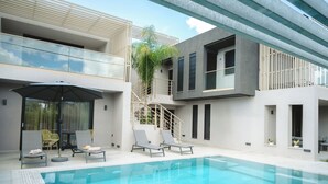 Ein moderner Poolbereich im Freien mit Liegestühlen und einem Tisch, umgeben von einem zweigeschossigen Gebäude mit großen Fenstern und einer Treppe.