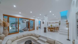 A spacious living area with a curved sofa, a dining table, and a staircase with a blue-lit landing. - "LARRI" - Architect & Luxurious 3BR - Canggu Beach (Bali)