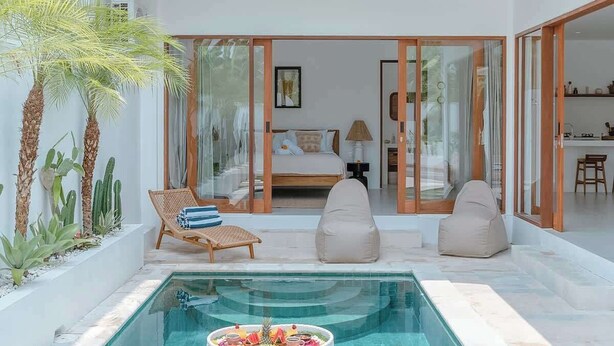 A modern indoor pool with a heart-shaped float, surrounded by a minimalist living area with a bed, seating, and a kitchen visible through glass doors. - "LARRI" - Architect & Luxurious 3BR - Canggu Beach (Bali)