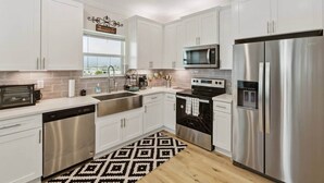 Una cocina moderna con armarios blancos, electrodomésticos de acero inoxidable, microondas, horno y lavavajillas.