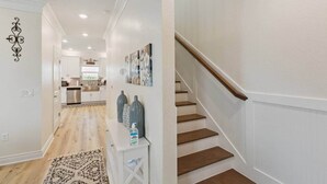 Un pasillo que conduce a una cocina con armarios blancos, piso de madera y una escalera con barandilla de madera.