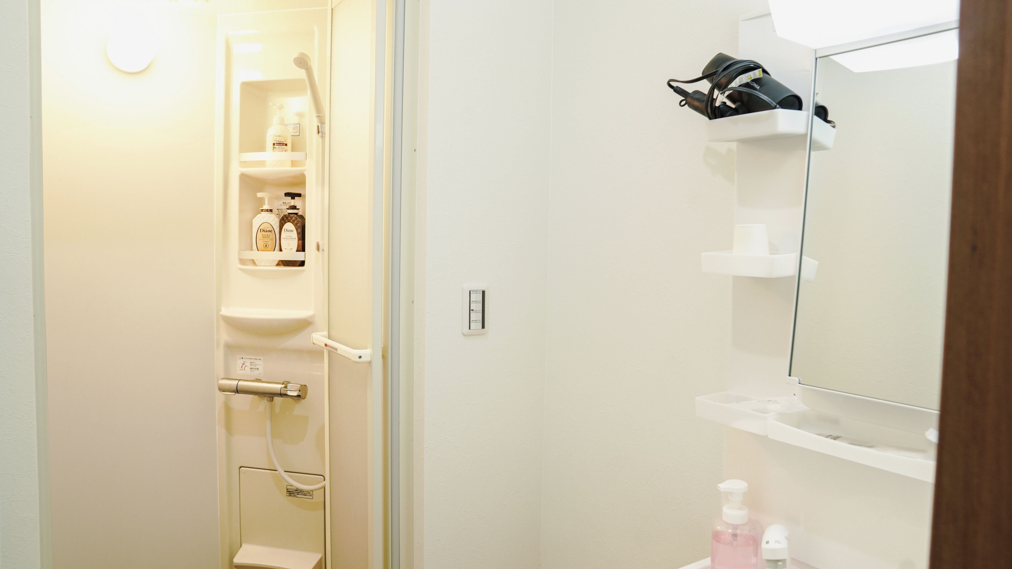 Une salle de bain avec une douche, un lavabo et un miroir. On trouve des articles de toilette sur les étagères.