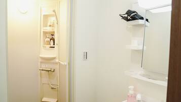 Une salle de bain avec une douche, un lavabo et un miroir. On trouve des articles de toilette sur les étagères.