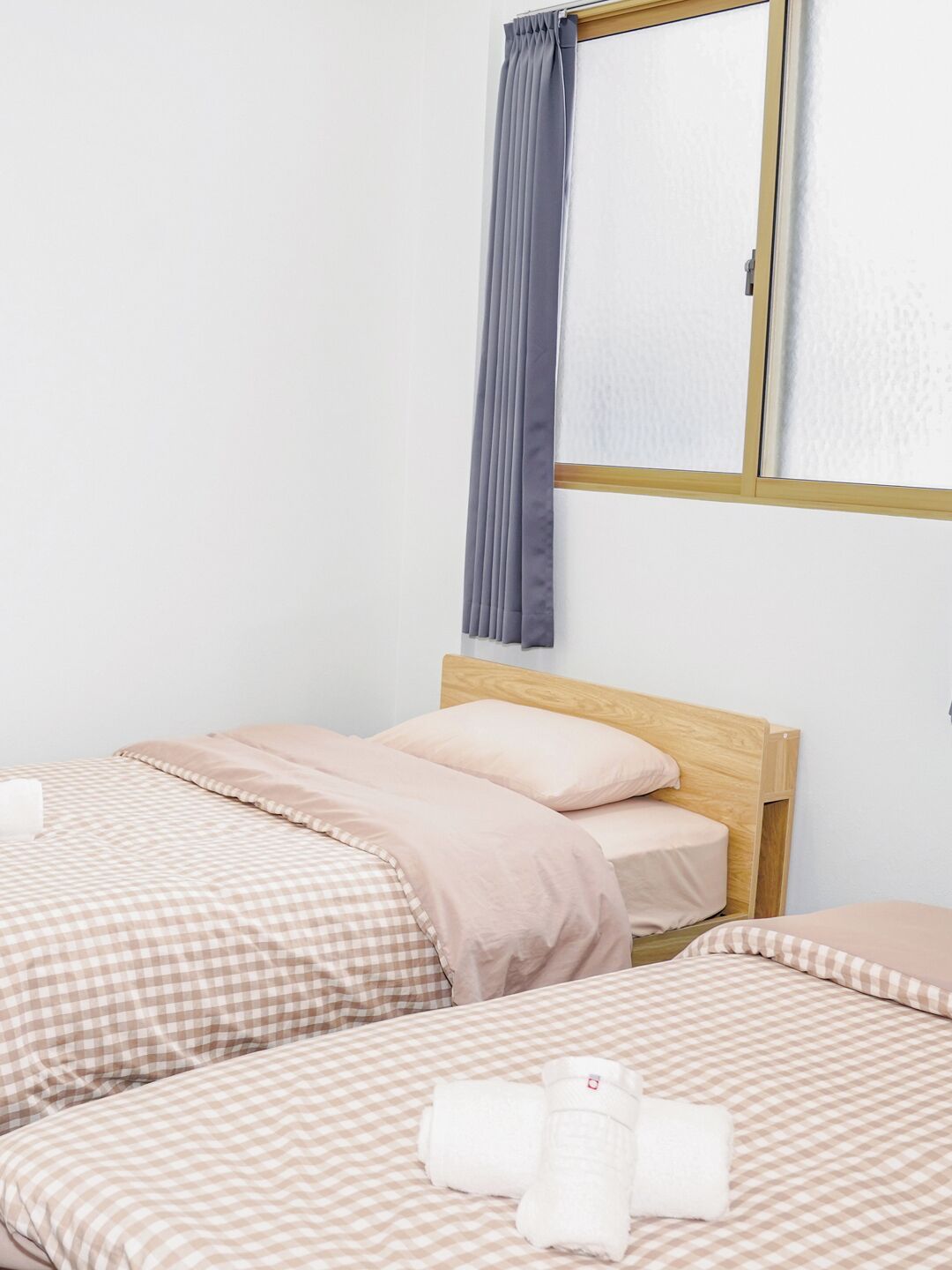 A bedroom with two beds, each with a wooden headboard, and a large window with a grey curtain.