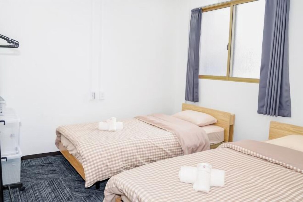 A hotel room with two beds, a desk, and a window with curtains.