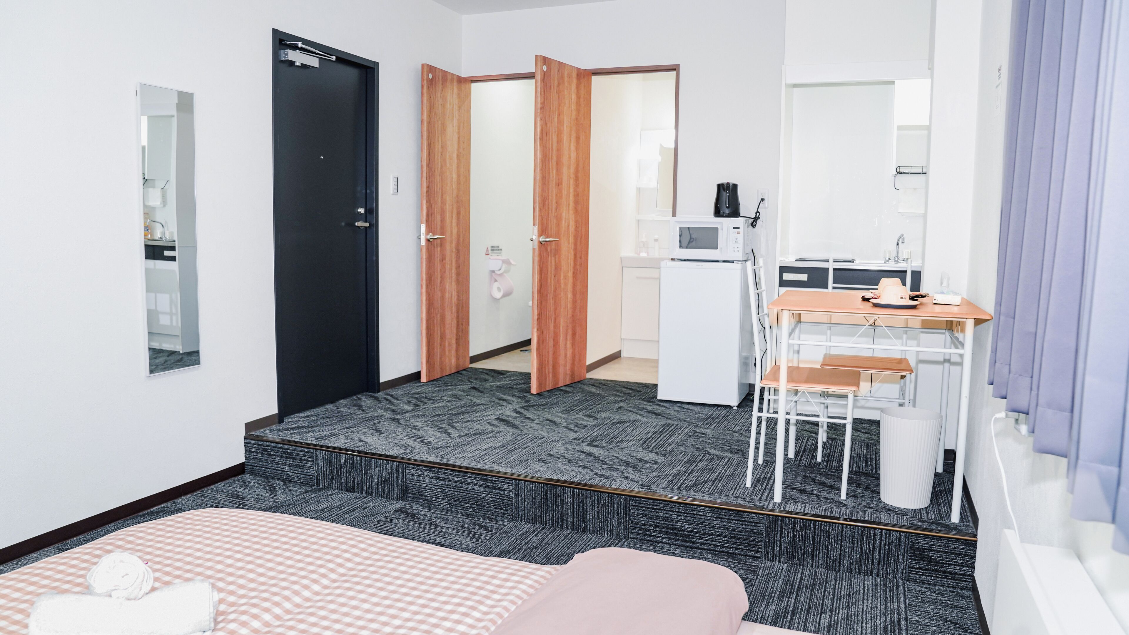 Quarto de hotel com cama, escrivaninha, micro-ondas e pequena copa.