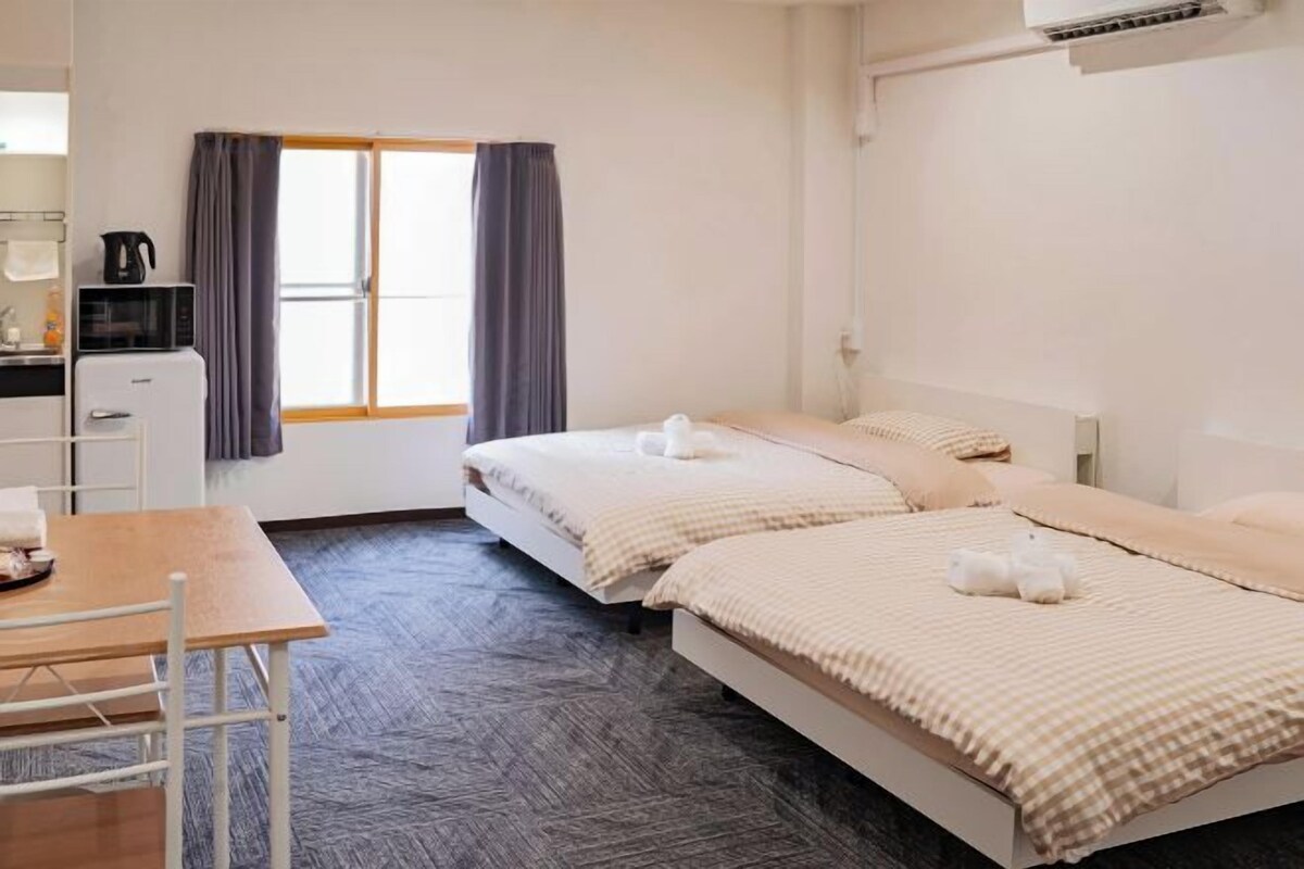 A hotel room with two beds, a small table, a microwave, and a refrigerator.