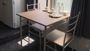 A compact kitchenette with a microwave and refrigerator, a small dining table with chairs, and a window with curtains. - Hoshi No Yado (Osaka)