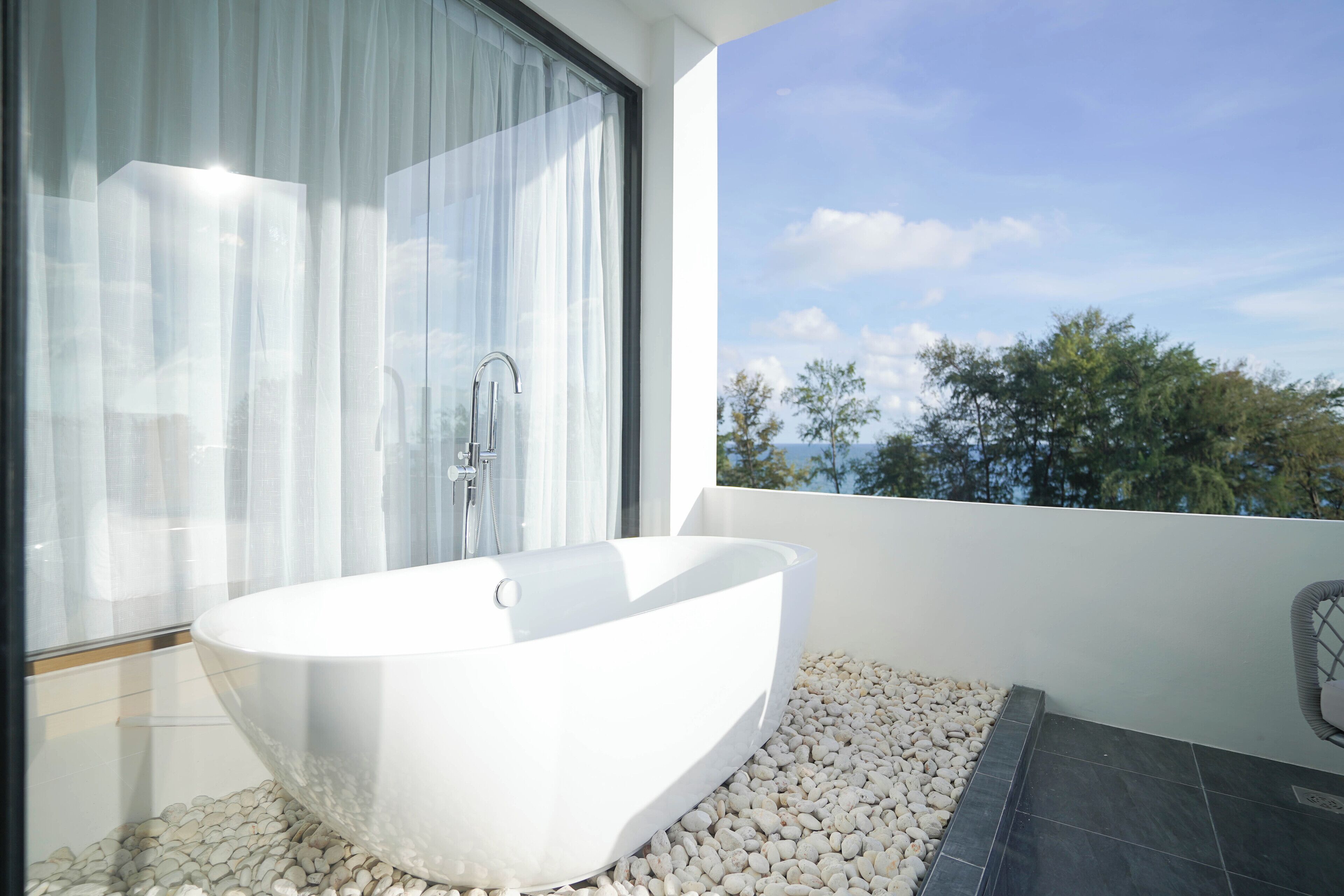 Un baño moderno con una bañera independiente, cabina de ducha con mampara de vidrio y vistas a árboles y cielo.
