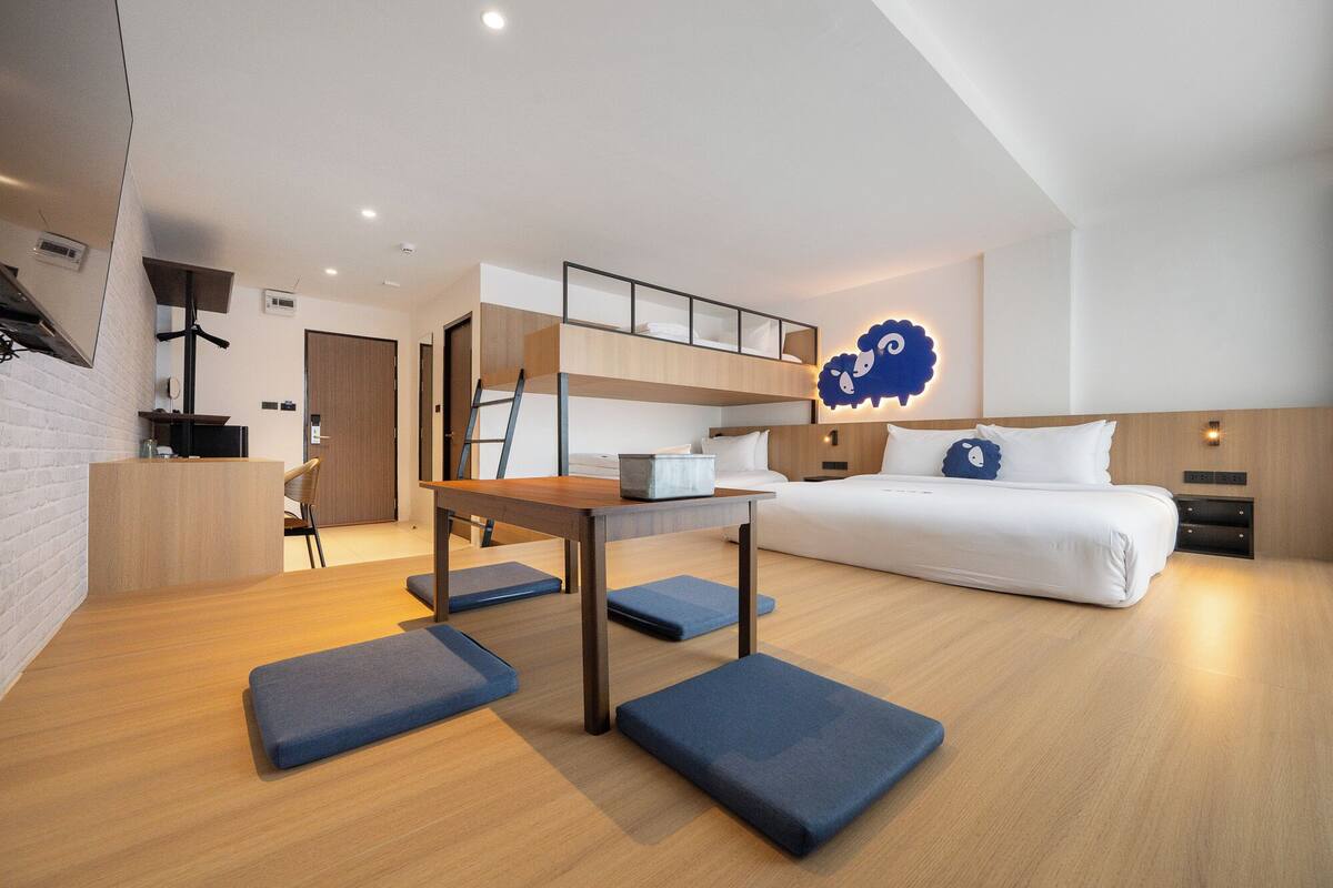 A modern hotel room with a bunk bed, a desk, and a small kitchenette.