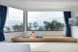 A modern bedroom with a large window, a bed, a small wooden table, and a TV mounted on the wall. - Kokotel Rayong Beachfront (Rayong)