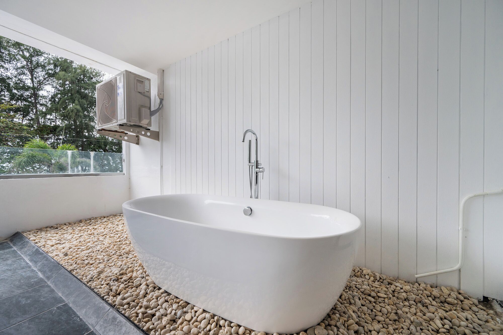 Ein modernes Badezimmer mit einer freistehenden Badewanne, einer Dusche und einem Fenster mit Blick auf Bäume.