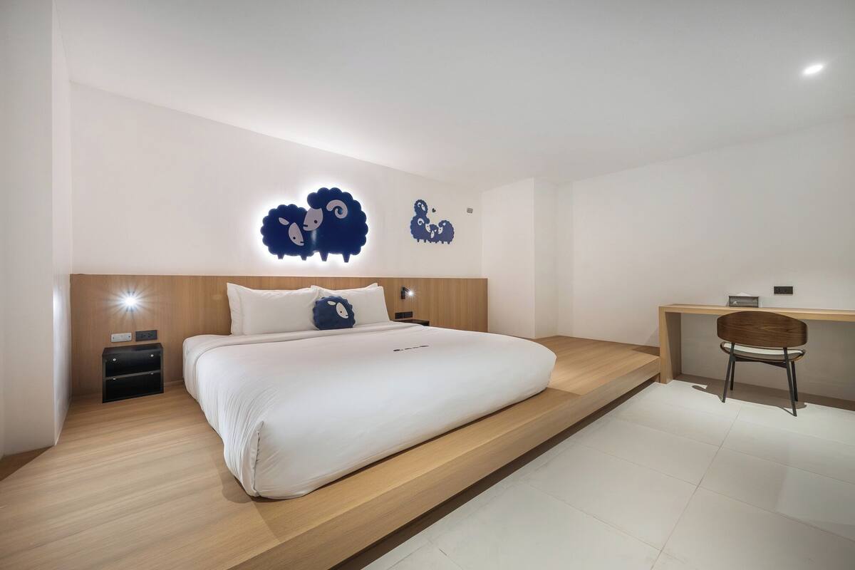 A modern bedroom with a large bed, a desk, and two wall-mounted light fixtures.
