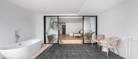 Une salle de bain moderne avec une baignoire îlot, un carrelage foncé et un espace recouvert de petits galets à côté de la baignoire.