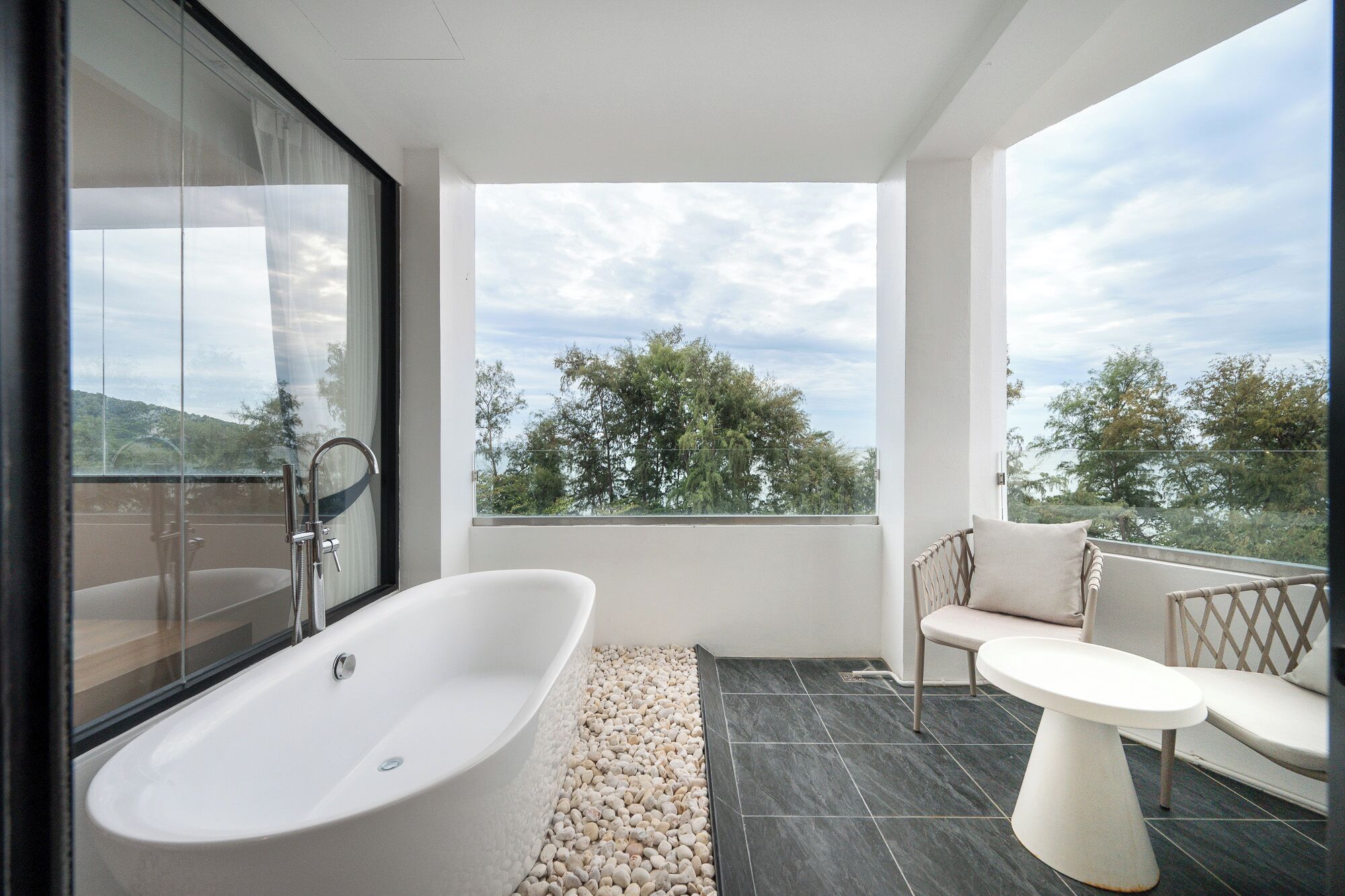Un baño moderno con una bañera independiente, cabina de ducha con mampara de vidrio y un balcón con mobiliario de exterior.
