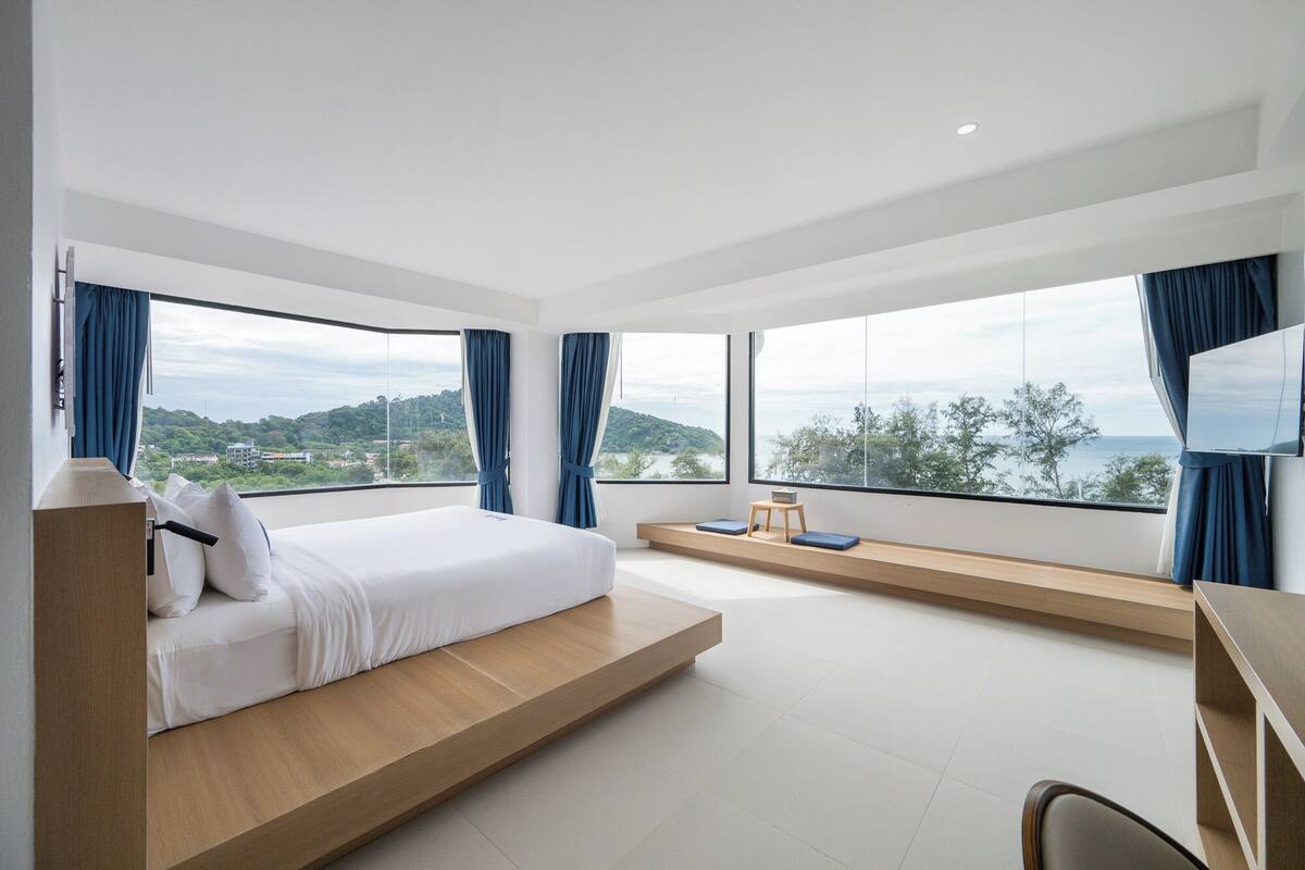 A modern bedroom with a bed, large windows, and a view of the landscape.