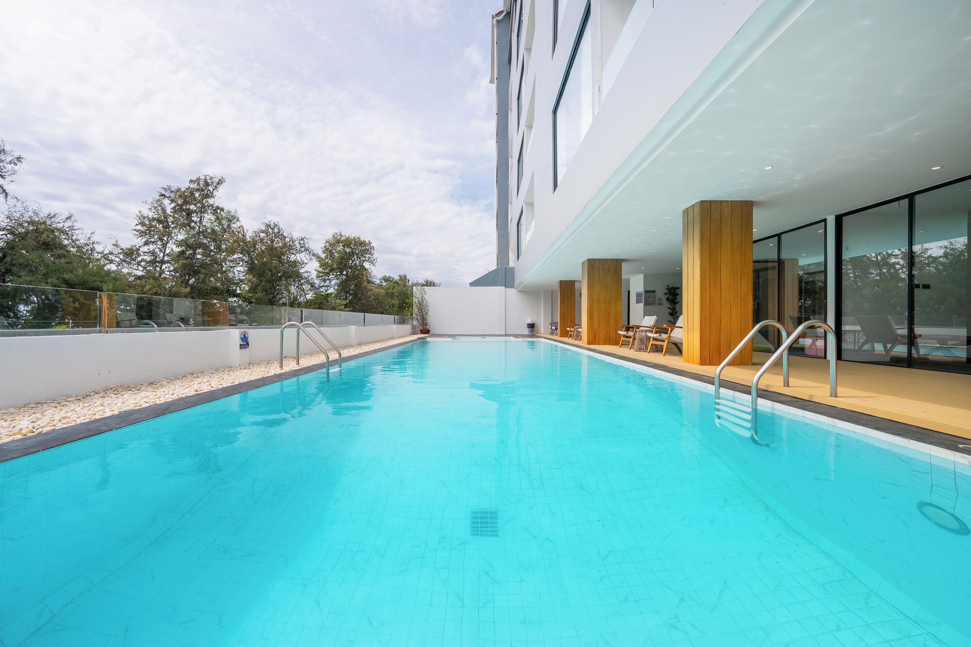 An indoor swimming pool with clear blue water, surrounded by a white wall and wooden pillars.