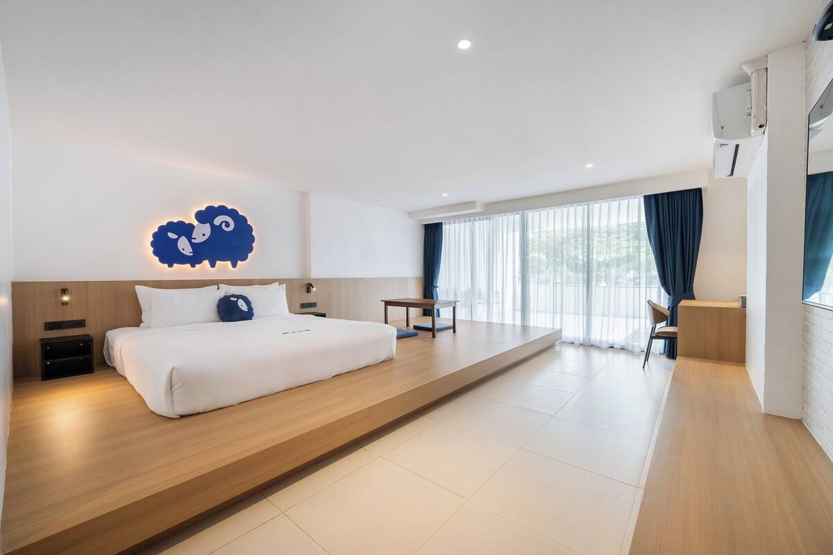 A modern hotel room with a large bed, a desk, and a seating area.