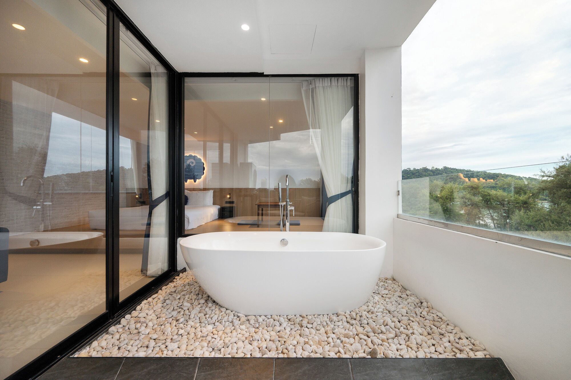 A modern bathroom with a freestanding bathtub, a glass shower enclosure, and a view of a natural landscape.