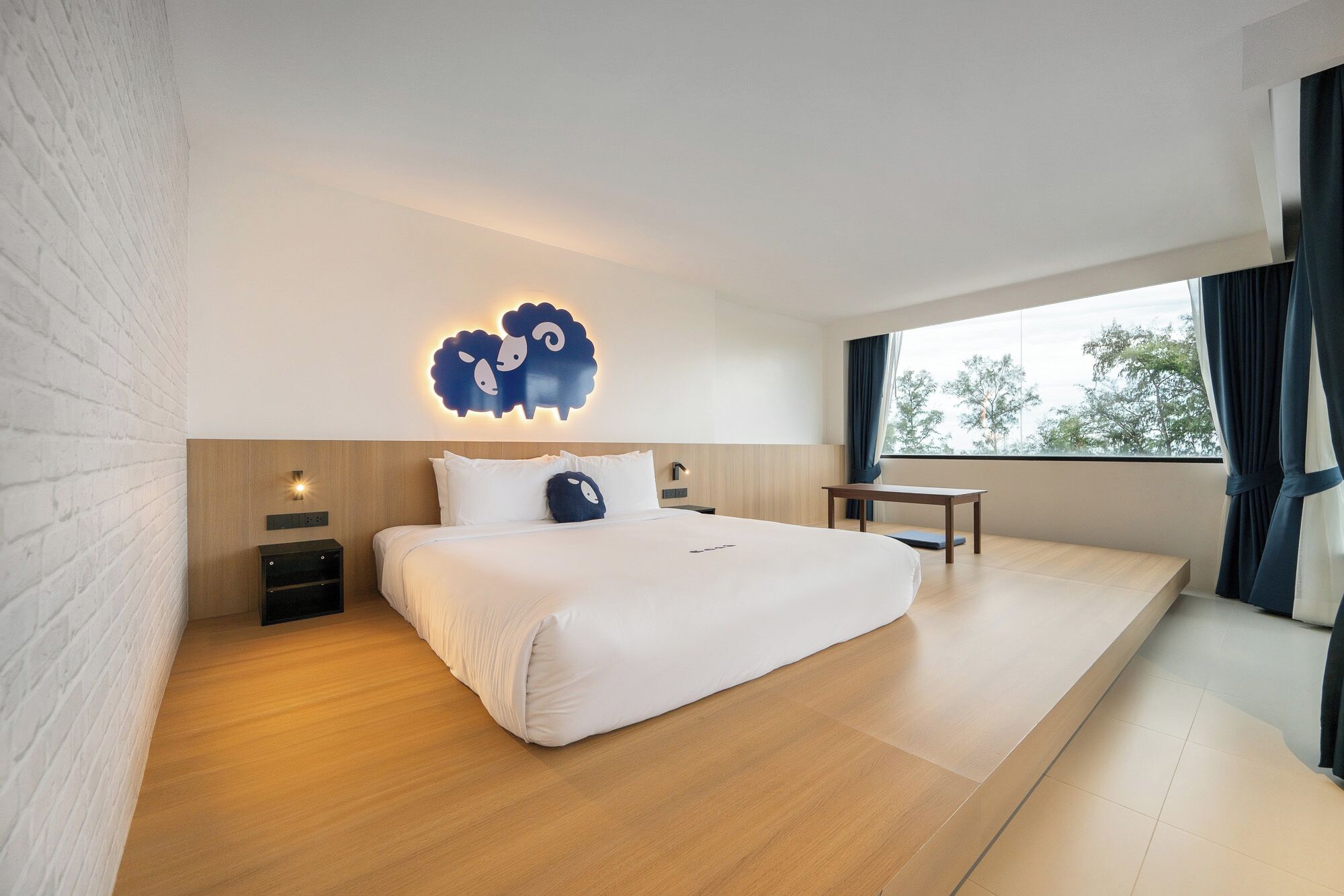 A modern hotel room with a large bed, a small desk, and a wall-mounted light fixture.