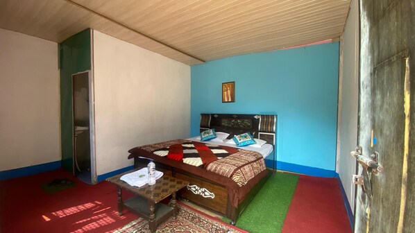 A bedroom with a bed, a wooden nightstand, a small table, a red carpet, and a green mat.