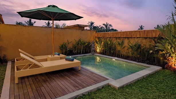 A pool area with lounge chairs and an umbrella, surrounded by greenery and palm trees. - Pelana Ubud Villa (Tegallalang)