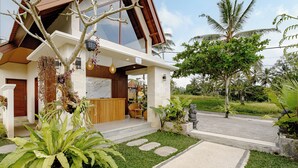 A modern house with a large glass window, a stone pathway, and a well-maintained garden with tropical plants. - Pelana Ubud Villa (Tegallalang)
