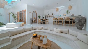Amplia sala de estar con un sofá curvo, una mesa de centro de madera y un comedor con sillas y mesa de madera.