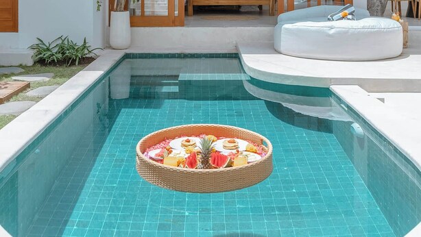Una casa moderna con piscina, terraza de madera y un espacio de descanso acogedor con cama y sofá.