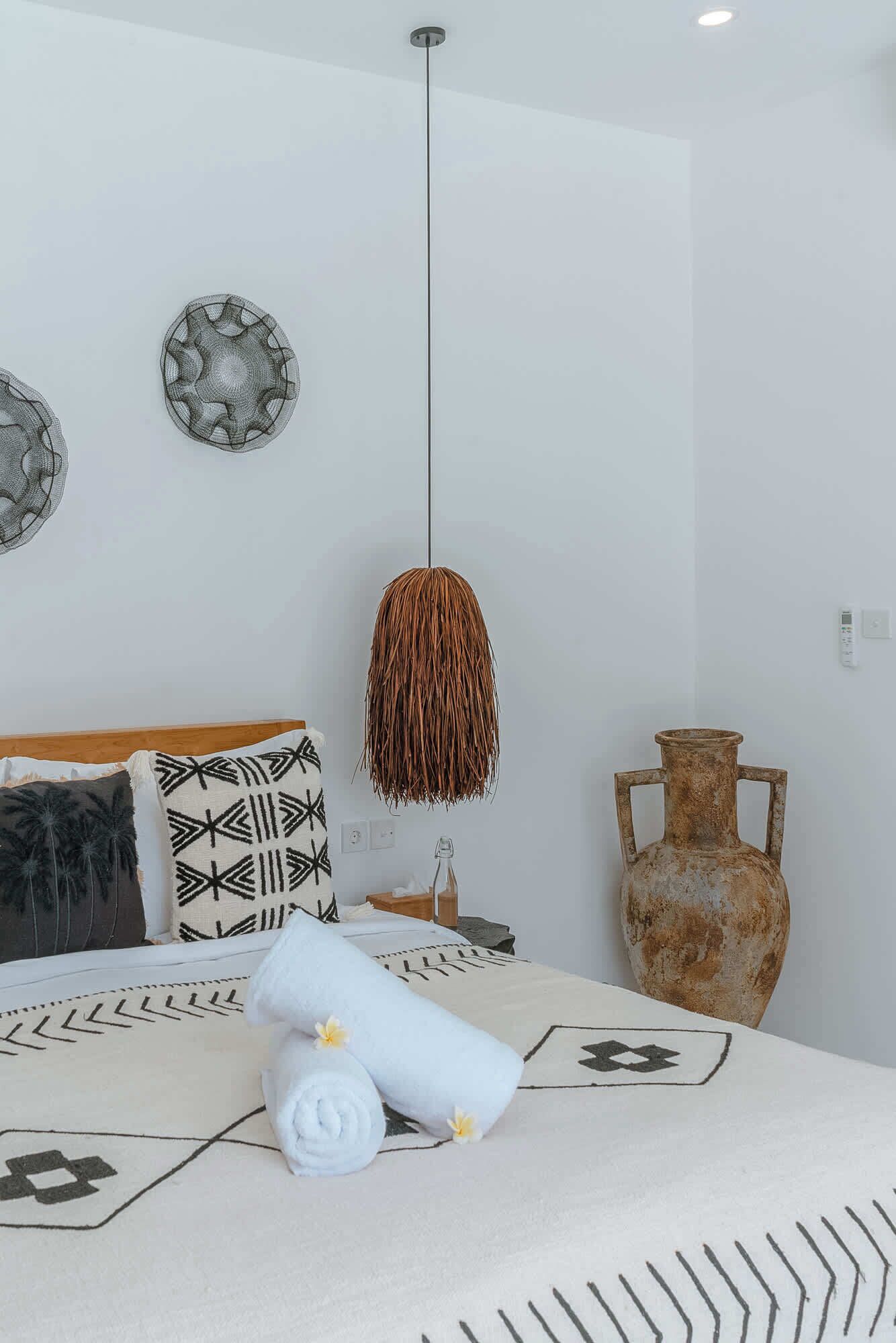 Une chambre à coucher avec un lit, une lampe suspendue, un vase et des assiettes décoratives accrochées au mur.
