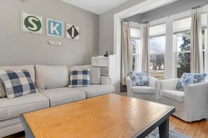 Ett vardagsrum med en soffa, fåtöljer, ett soffbord och ett fönster med gardiner.