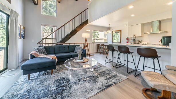 A modern living room with a sofa, coffee table, and bar stools. A staircase leads to an upper level. - Cozy lofted condo in Kings Beach close to everything! (Kings Beach)