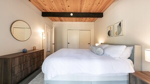 A bedroom with a wooden ceiling, a large bed with white bedding, a dresser, a mirror, and a door. - Cozy lofted condo in Kings Beach close to everything! (Kings Beach)